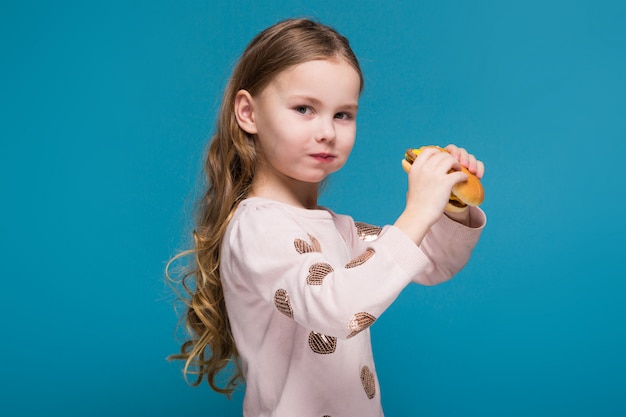 Hübsches, kleines Mädchen in der Strickjacke mit dem Brunethaar halten einen Burger