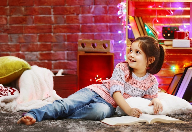 Hübsches kleines Mädchen mit Buch im weihnachtlich dekorierten Raum