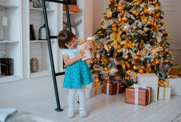 Hübsches kleines Mädchen öffnet ein Weihnachtsgeschenk. Porträt des glücklichen Kindes am Weihnachtsabend.