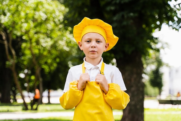 Hübsches Kochkind in gelber Kochmütze und Schürze gelbe Uniform posiert im Freien Kreative Werbung für Lebensmittelgeschäft und Café