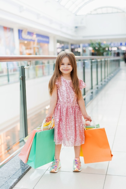 Hübsches lächelndes kleines Mädchen mit Einkaufstüten, die im Geschäft aufwerfen. Schöne süße Momente der kleinen Prinzessin, hübsches freundliches Kind, das Spaß hat