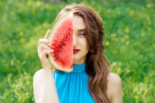 Hübsches Mädchen bedeckt einen halben Teil ihres Gesichts mit einer Scheibe Wassermelone in der Natur.