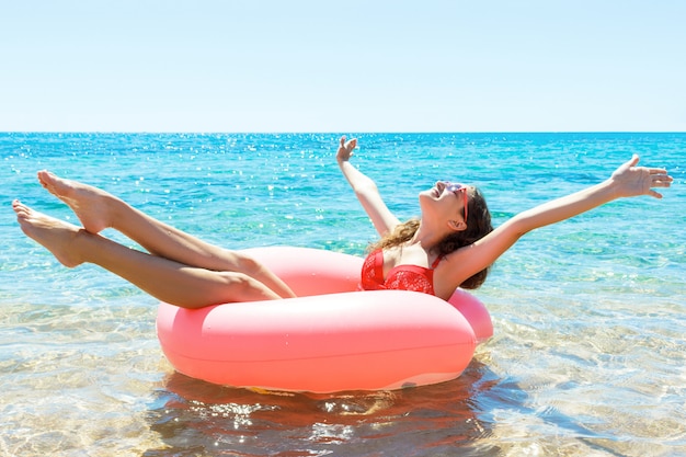 Hübsches Mädchen hat Spaß auf einem rosa aufblasbaren Ring im Meer