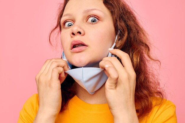 Hübsches Mädchen in einem gelben T-Shirt medizinische Maske Schutz rosa Hintergrund unverändert