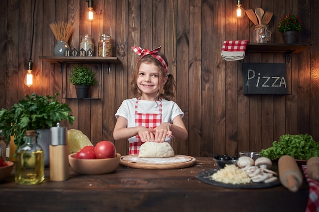 Hübsches Mädchen in knetendem Brotteig des karierten Schutzblechs für Pizza