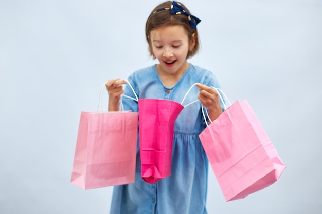 Hübsches Mädchen in lässigem Jeanskleid hält rosa Einkaufstaschen in der Hand