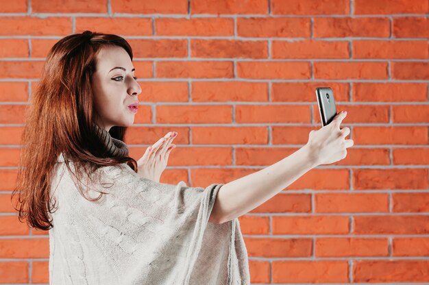 hübsches Mädchen macht Selfie mit dem Smartphone und sendet Luftkuß, halbe Gesichtsansicht