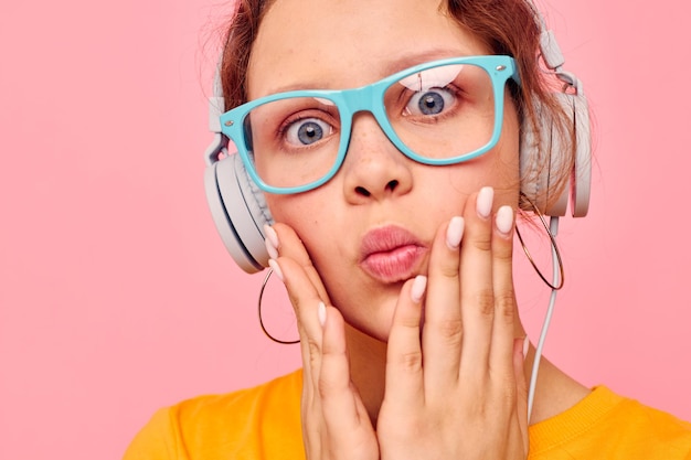 Hübsches Mädchen mit blauer Brille, das Musik auf Kopfhörern hört, rosa Hintergrund unverändert