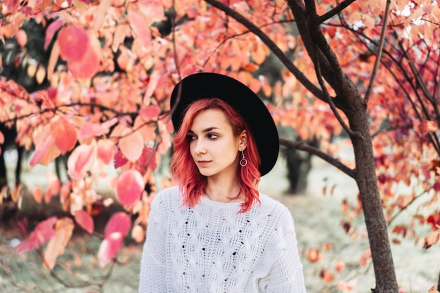 Hübsches Mädchen mit dem roten Haar und Hut gehend in den Park, Herbstzeit.