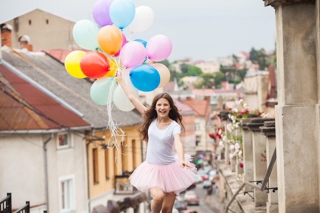 Hübsches Mädchen mit großen bunten Latexballons posiert auf der Straße einer Altstadt