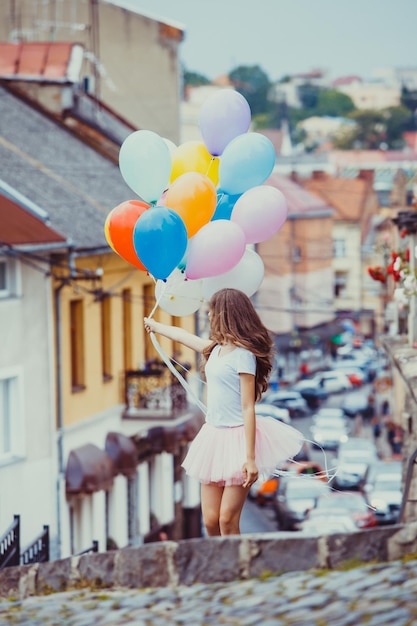 Hübsches Mädchen mit großen bunten Latexballons posiert auf der Straße einer Altstadt