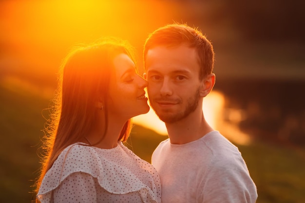 Hübsches Mädchen will ihren Freund auf einem Hintergrund von Sonnenuntergang und See auf die Wange küssen