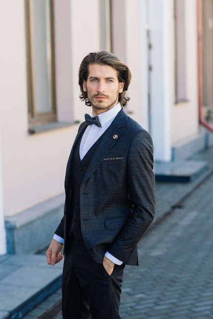 Hübsches Modegeschäftsmann-Modell, gekleidet in einem eleganten Anzug und posiert auf der Straße. Metrosexuell