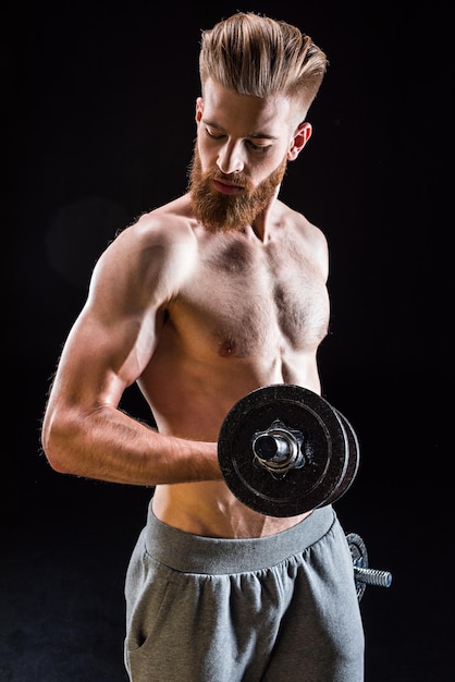 Hübsches muskulöses Bodybuildertraining mit Hantel isoliert auf schwarz