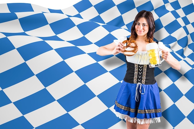 Hübsches oktoberfest-mädchen, das bierkrug und brezel gegen blau-weiße flagge hält