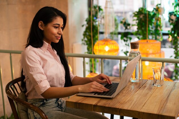 Hüfte einer hübschen jungen Dame, die allein am Cafétisch sitzt und lächelt, während sie an einem modernen Laptop arbeitet working