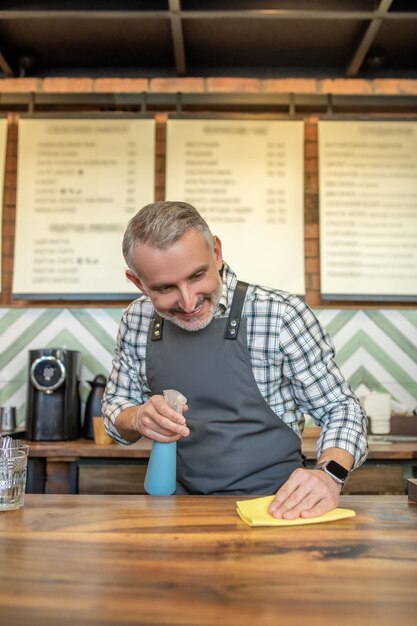 Hüftporträt eines lächelnden Café-Mitarbeiters, der die Arbeitsplatte mit einem feuchten Tuch abwischt