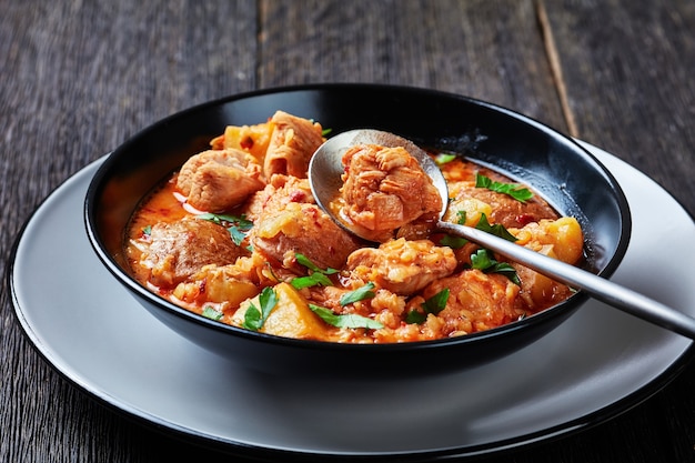 Hühnchen-Arrabbiata-Eintopf mit Linsen und Kartoffeln in einer Schüssel auf einem Holztisch, horizontale Ansicht von oben, Nahaufnahme