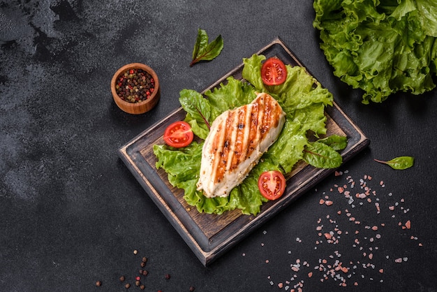 Hühnchen-, Tomaten- und Salatblätter auf dunklem Betonhintergrund. Leckeres gesundes Essen