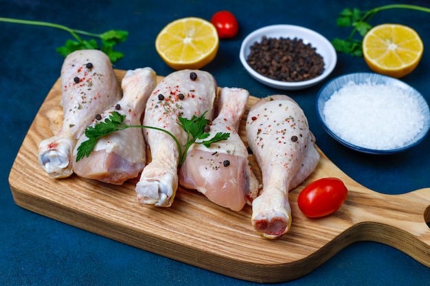 Hühnerbeine mit Gewürzen und Salz bereit zum Kochen auf Schneidebrett.