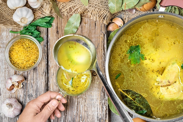 Hühnerbrühe mit Gemüse und Gewürzen in einem Topf, Zutaten für die Suppe auf einem Holztisch