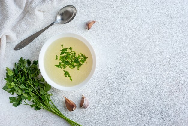 Hühnerbrühe mit Petersilie in der Schüssel auf weißem Tisch, Draufsicht