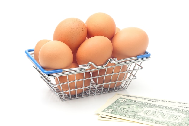 Hühnereier in einem Supermarkt-Einkaufskorb und Dollars auf einem weißen Hintergrund. Verkauf und Geschäft von Lebensmitteln