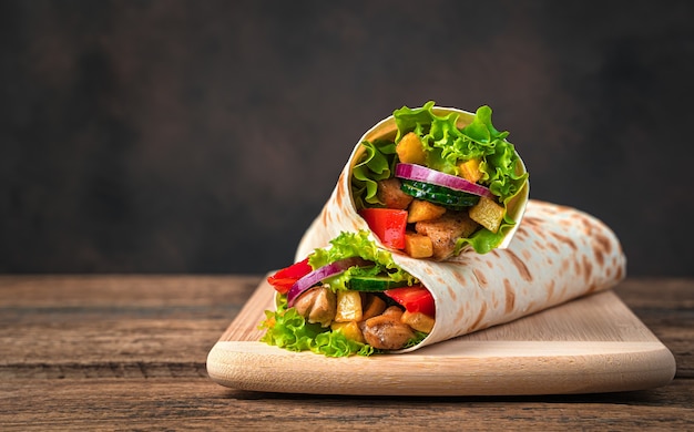 Hühnerfleisch, Pommes frites, Gemüse und Salat werden in Fladenbrot an einer braunen Wand gewickelt. Traditionelles Schawarma. Seitenansicht, Kopienraum.