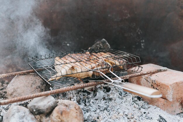 Hühnerfleisch wird am Grill auf schwelenden Kohlen oder Glut von einem Lagerfeuer auf dem Boden am Sommer- oder Herbsttag grillen unter Campingbedingungen gebraten, um auf dem Land und im wilden Landleben zu überleben