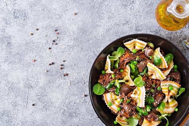 Hühnerherzen mit Karotten in süß-saurer Sauce mit Farfalle-Nudeln. Gesunder Salat. Draufsicht. Flach liegen.