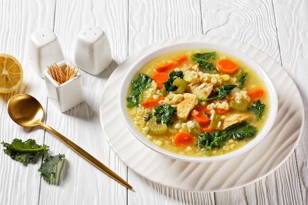 Hühnerkohlsuppe mit Pasta Anellini und Gemüse in einer weißen Schüssel mit goldenem Löffel auf einem Holztisch, italienische Küche