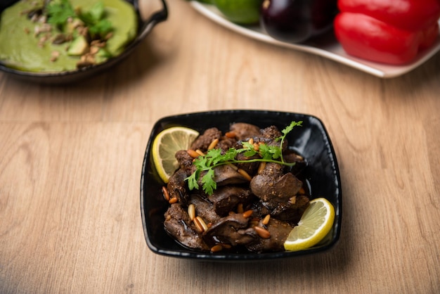 Hühnerleber-Masala mit Zitronenscheibe, serviert in einer Schüssel, die auf dem Tisch mit Blick auf arabisches Essen isoliert ist