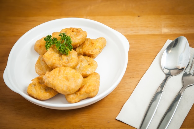 Hühnernuggets in der weißen Schüssel nahe Gabel und Löffel auf einem hölzernen Hintergrund.