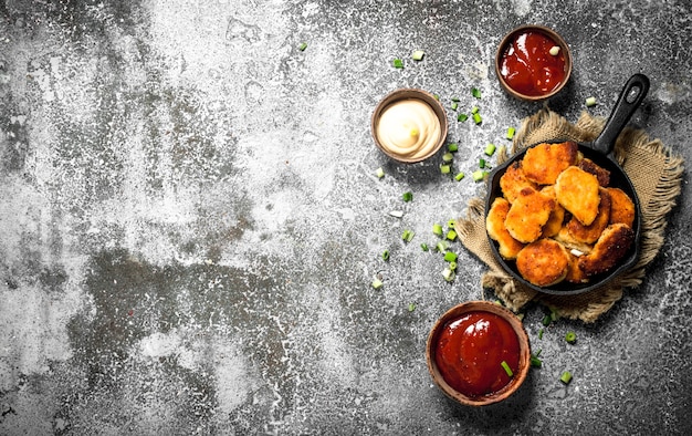 Hühnernuggets in einer Pfanne mit verschiedenen Saucen. Auf einem rustikalen Hintergrund.