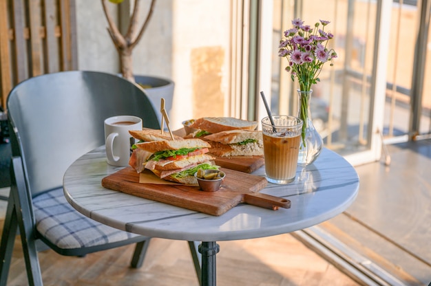 Hühnersandwich mit Eiskaffee und Blumenvase auf dem Tisch im Café