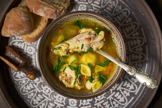 Hühnersuppe in einer Tonschale, Brot, Draufsicht.