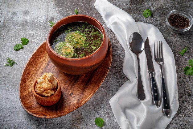 Hühnersuppe mit gekochtem Ei, bestreut mit Dill und Petersiliengrün in einer Holzschüssel mit Semmelbrösel steht isoliert auf einem Steintisch, Flatlay