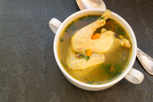 Hühnersuppe mit Gemüse auf einem schwarzen Hintergrund.