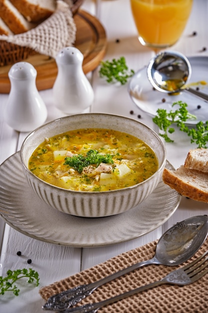 Hühnersuppe mit knusprigem Brot und Orangensaft auf einem weißen Holztisch Nahaufnahme