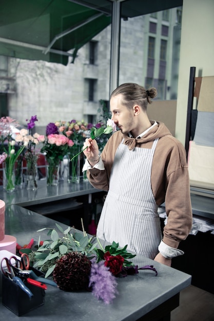 Huele bien. Apuesto joven vistiendo delantal mientras trabajaba en la tienda de flores