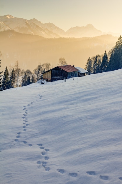 Huellas en la nieve hacia cabaña de madera en las montañas de Allgau