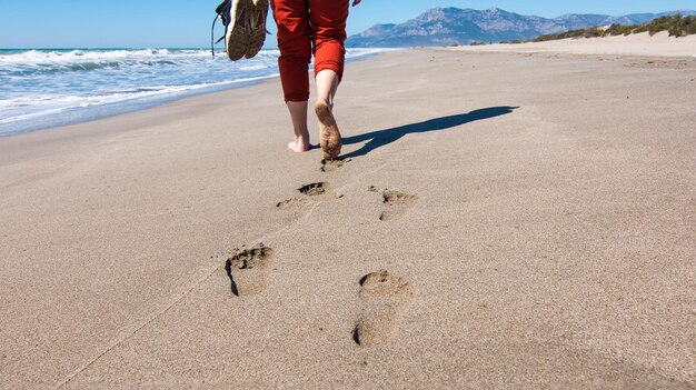 Huellas en el pie de arena de una niña caminando con zapatillas en la mano Niña corriendo con un perro en la playa de Patara Turquía