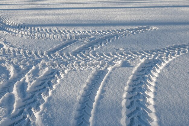 Huellas de un tractor de ruedas en la nieve en el campo. Patrones de nieve de invierno