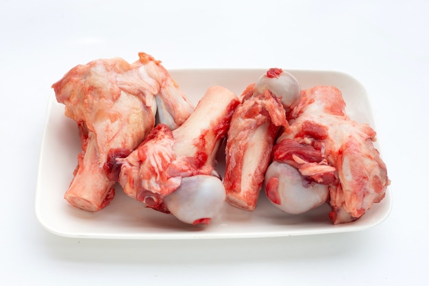 Huesos de cerdo crudos en plato blanco sobre fondo blanco.