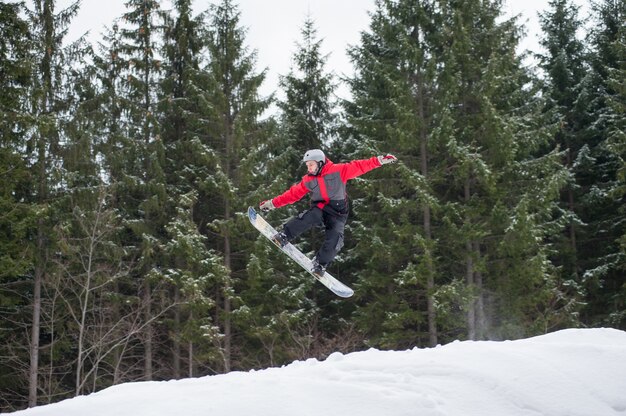 Huésped masculino en la tabla de snowboard saltando sobre la pendiente