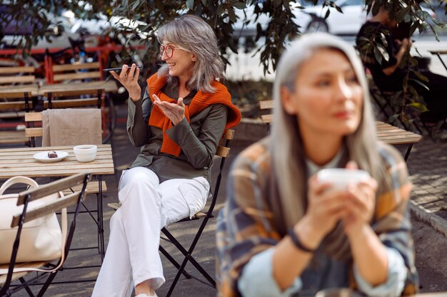 Los huéspedes del café senior se centran en la mujer de pelo plateado con gafas grabando un mensaje de audio