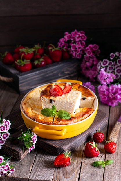 Hüttenkäse-Auflauf mit Rosinen und Erdbeeren in einer Auflaufform auf hölzernem Hintergrund. Gesundes Frühstück