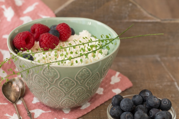 Hüttenkäse in blauer Schüssel mit Himbeeren und Blaubeeren auf Holz