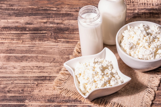 Hüttenkäse in einer Keramikschale mit Milch in Flaschen. Hausgemachtes Milchprodukt auf einem tiefen Teller. Alter Holztisch, Kopierraum