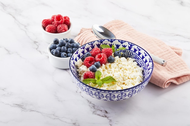 Hüttenkäse in Schüssel dekoriert mit Himbeeren und Heidelbeeren und Minzblättern auf weiß